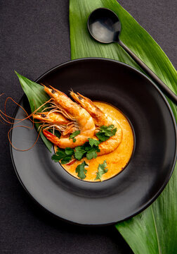Seafood cream soup with shrimps in black plate, on black background. Top view