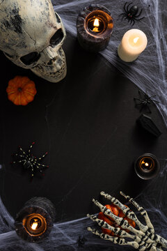 Happy Halloween skull and skeleton hand with pumpkin, candlelight, spider and cobweb horror still life on vertical dark background