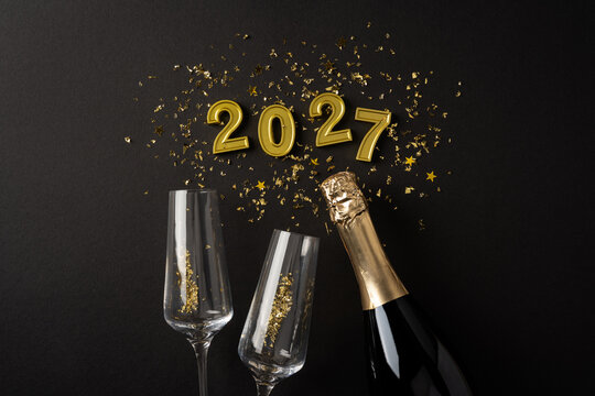 Happy New Year 2027 celebration with champagne bottle, two glasses and gold confetti