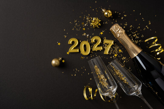 Happy New Year 2027 celebration with champagne bottle, glasses and gold confetti on black background