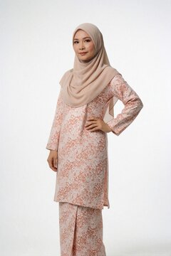 Young Malay woman wears traditional baju kurung dress with floral pattern, beige tudung headscarf. Female stands posing against plain white studio background. Adult lady models modest Islamic fashion
