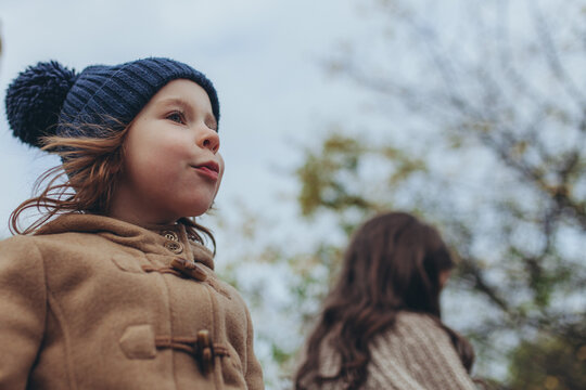 Portrait of brave little girl with curious expression, wearing warm coat and blue beanie, standing outdoors on windy autumn day. Spirit of exploration, feelings of freedom, discovery, childhood wonder