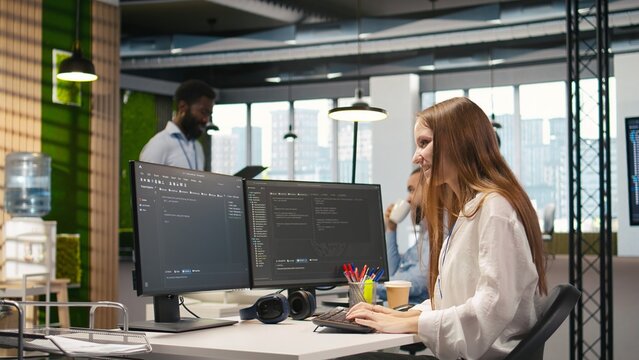 Young female programmer writes code and develops machine learning APIs, troubleshooting software errors and faults with artificial intelligence while working on a computer in a startup office.