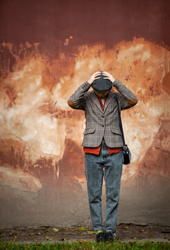 Distressed woman or man in vintage tweed fashion standing alone against a textured wall, holding head in hands in a powerful expression of despair, hopelessness, and emotional turmoil