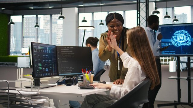 Happy manager praises an intern with encouraging words and a congratulatory high five, giving positive feedback, motivation and support to a young female engineer after progress at work.