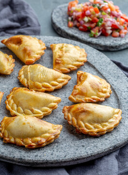 Cocktail empanadas on stone plate with tomato sauce and guacamole . Gray background. Latin American and Spanish tipical food