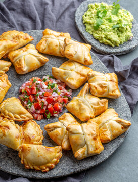 Cocktail empanadas on stone plate with tomato sauce and guacamole . Gray background. Latin American and Spanish tipical food