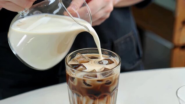 Ultra smooth 4K beverage video capturing fresh creamy milk being poured into a glass of iced coffee creating a beautiful swirling marble pattern with rich contrast
