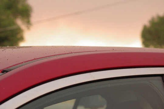 Close-up of ashes from a nearby wildfire landing on the roof of an automobile beneath a yellow-tinted, smoky sky.