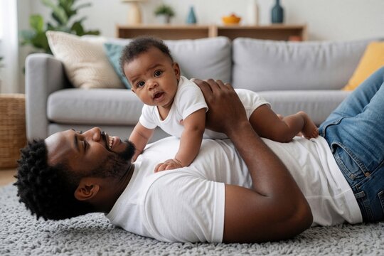 Happy African American father lies on floor with infant son. Black dad cuddles cute baby boy on chest at home. Young parent spends time with small child in living room during paternity leave. Joyful