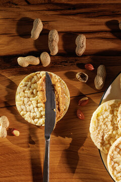 Spreading Peanut Butter On Rice Cake With Knife On Wooden Table