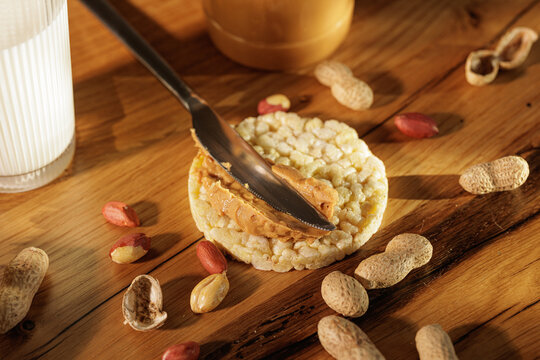 Spreading Peanut Butter On Rice Cake With Peanuts And Milk