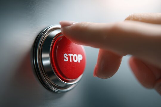 A finger pressing a red stop button on a metallic surface signaling an urgent command to halt or pause a machine or process