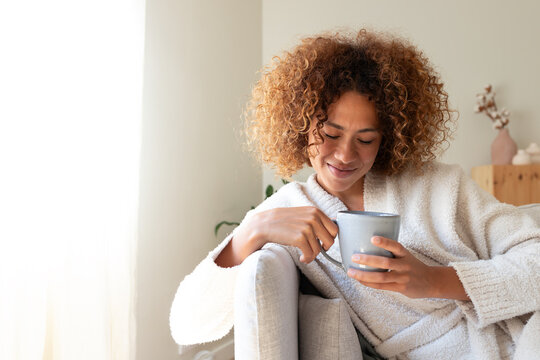 Woman enjoying warm drink looking down in robe