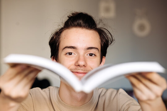 Smiling teenager flipping book pages toward camera