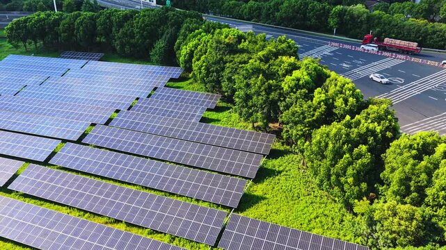 Aerial lateral movement over solar panels beside a tree lined road