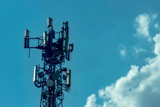 Metal telecommunication tower silhouette. Cellular antennas stands tall against a vibrant blue sky with soft white clouds, representing modern connectivity and network communication.