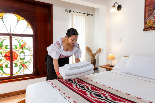 Indigenous Kichwa woman in traditional clothing arranging fresh white towels on a bed in a hotel room