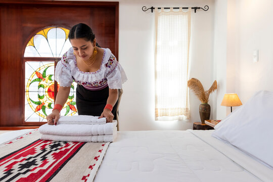 Indigenous Kichwa woman in traditional clothing arranging fresh white towels on a bed in a hotel room