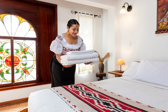 Indigenous Kichwa woman in traditional clothing arranging fresh white towels on a bed in a hotel room