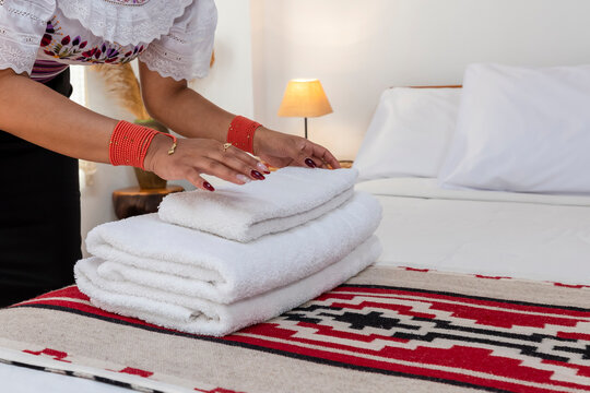 Indigenous Kichwa woman in traditional clothing arranging fresh white towels on a bed in a hotel room