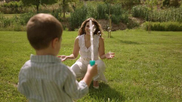 Mother and son blowing soap bubbles in a sunny park