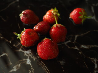 Fresh ripe strawberries on dark marble surface with dramatic natural light - arranged on a dark marble surface, illuminated by dramatic natural light with rich texture and vibrant red color. © Bluemoment72