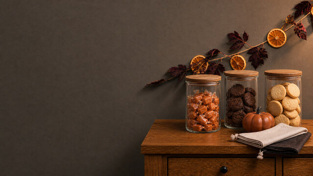 Glass jars of caramels and cookies on a wooden sideboard with a dried orange and autumn leaf garland, ガラス瓶のキャラメルとクッキー ドライオレンジと紅葉のガーランド