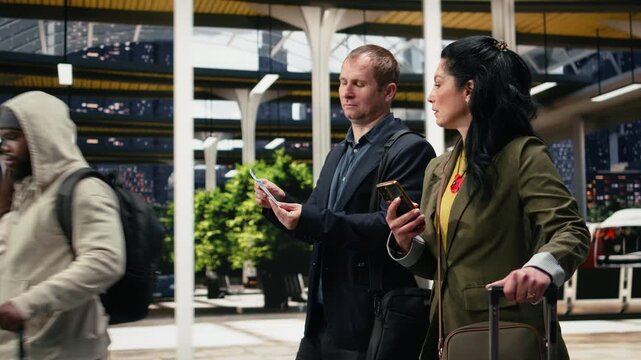 Business travelers compare a printed bus ticket with information on a smartphone inside a terminal; the companions review boarding pass details and mobile navigation before departure.