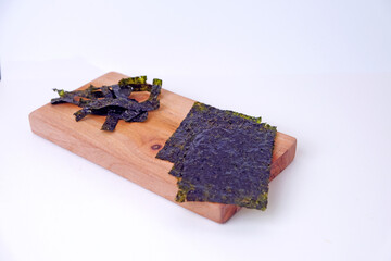 Dried crispy seaweed rests on a wooden board. Plates showcase texture and color, natural and rustic. Simple background highlights the seaweed's earthy tones. Perfect for food, health © Nurma