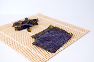 Dried seaweed rests on bamboo mat. Dark, textured sheets display natural color. Simple background highlights the product's purity. Ideal for health, wellness, or Asian cuisine themes © Nurma