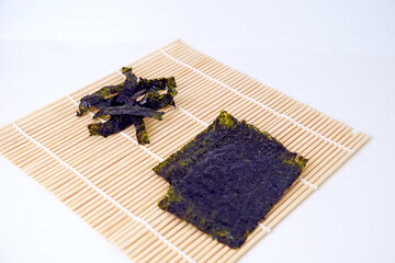 Dried seaweed rests on bamboo mat. Dark, textured sheets display natural color. Simple background highlights the product's purity. Ideal for health, wellness, or Asian cuisine themes © Nurma
