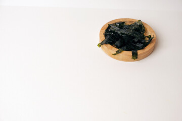 Dried seaweed rests in a simple wooden bowl. Minimalist background highlights texture and natural color. Clean white surface emphasizes products organic quality. Ideal for health, wellness © Nurma