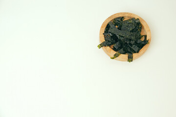 Dried seaweed rests in a simple wooden bowl. Minimalist background highlights texture and natural color. Clean white surface emphasizes products organic quality. Ideal for health, wellness © Nurma