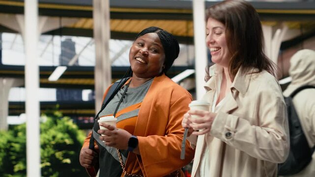 Friends carry drink cups through the coach station and discuss travel plans while enjoying conversation and refreshments in the bus station.