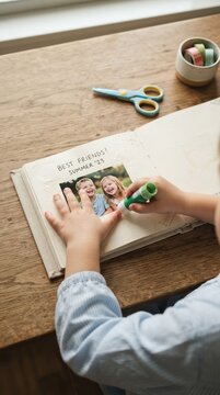 Young girl gluing photo into scrapbook on wooden table, memory book crafting concept