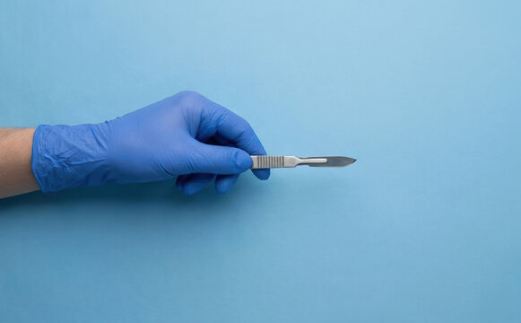 Gloved surgeon holding a surgical scalpel on a blue background representing medical procedure