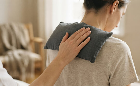 Young adult woman receiving a warm herbal compress on her upper back for neck pain relief