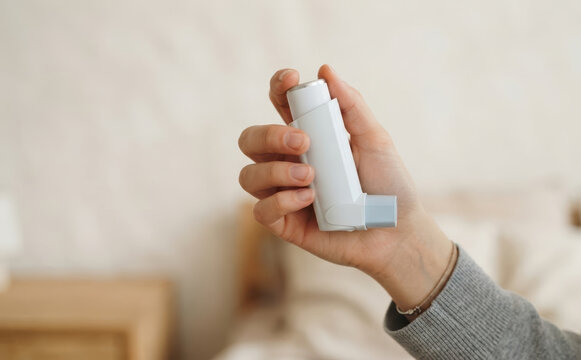 Young adult woman holding an inhaler for asthma treatment and breathing relief, close-up shot