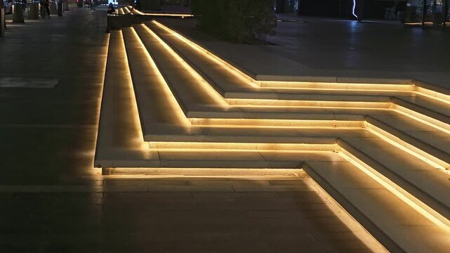 Illuminated zig-zag steps with warm LED strip lighting in a modern public plaza.