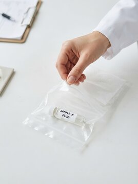 Scientist sealing a labeled sample vial in a plastic bag on a table in a research laboratory