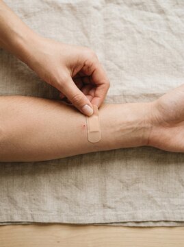 Applying adhesive bandage on forearm of adult Caucasian woman covering small injection wound