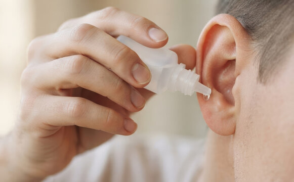 Man applying medical ear drops into his ear canal for infection treatment and health care close up