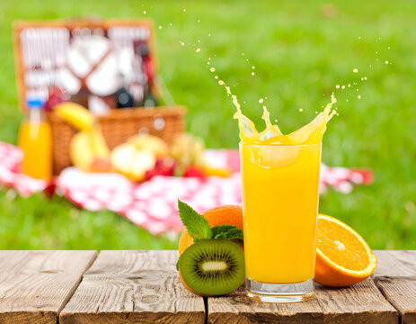 A glass of orange juice splashing on a wooden table with kiwi and oranges.