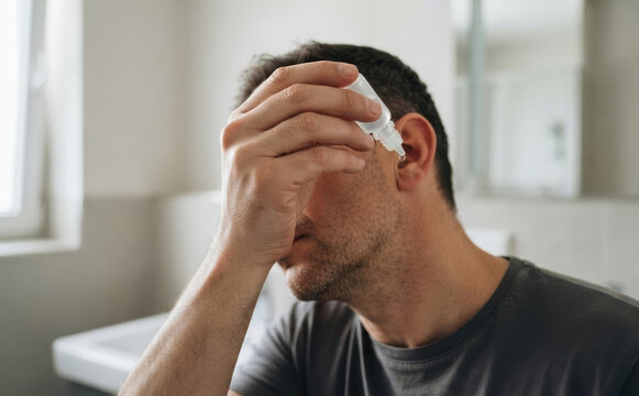 Middle-aged caucasian man using ear drops to treat earache at home, healthcare and medical concept