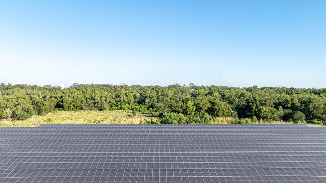Large solar farm with rows of photovoltaic panels set against a backdrop of lush green forest and distant mountains in Itaguai, Rio de Janeiro, Brazil. Aerial view.