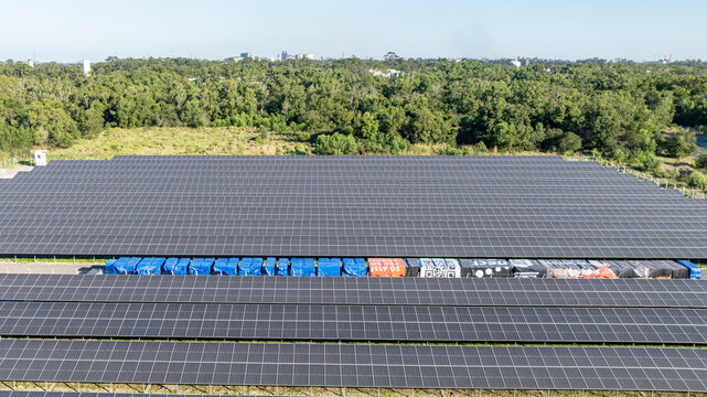 Large solar farm with rows of photovoltaic panels set against a backdrop of lush green forest and distant mountains in Itaguai, Rio de Janeiro, Brazil. Aerial view.
