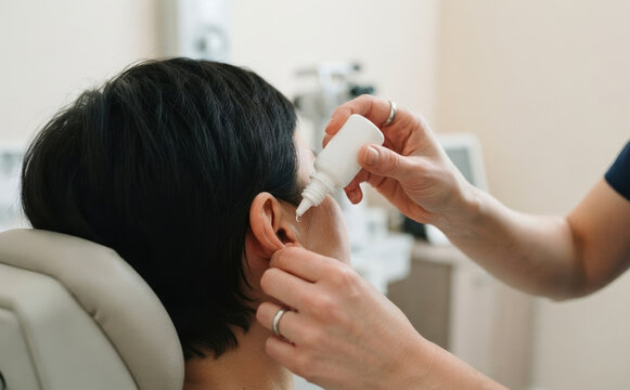 Doctor applying ear drops to adult female patient in a medical clinic for treatment