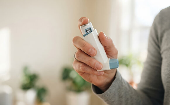 Close up of an adult woman holding an asthma inhaler to treat respiratory condition and breathing difficulty at home