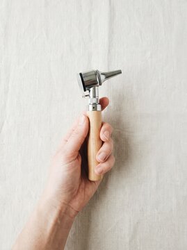 A person holding a vintage wooden handle medical otoscope diagnostic instrument on a white fabric background